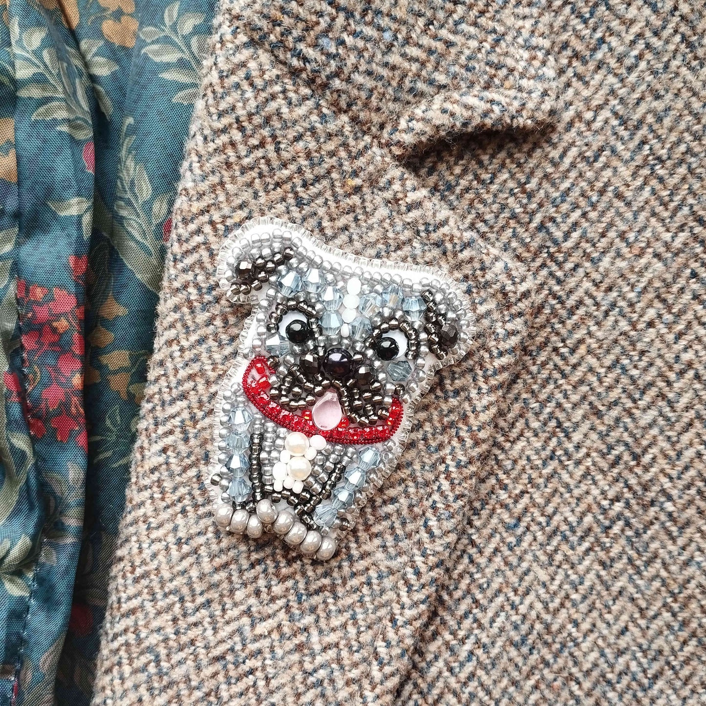 A close-up image of a grey dog embroidered on a tweed jacket, with a red ribbon around its neck.
