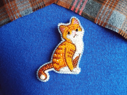 A close-up image of a cat embroidered on a blue fabric, with a plaid fabric visible in the background.