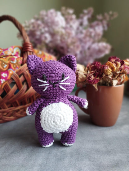 a crocheted cat next to a basket of flowers