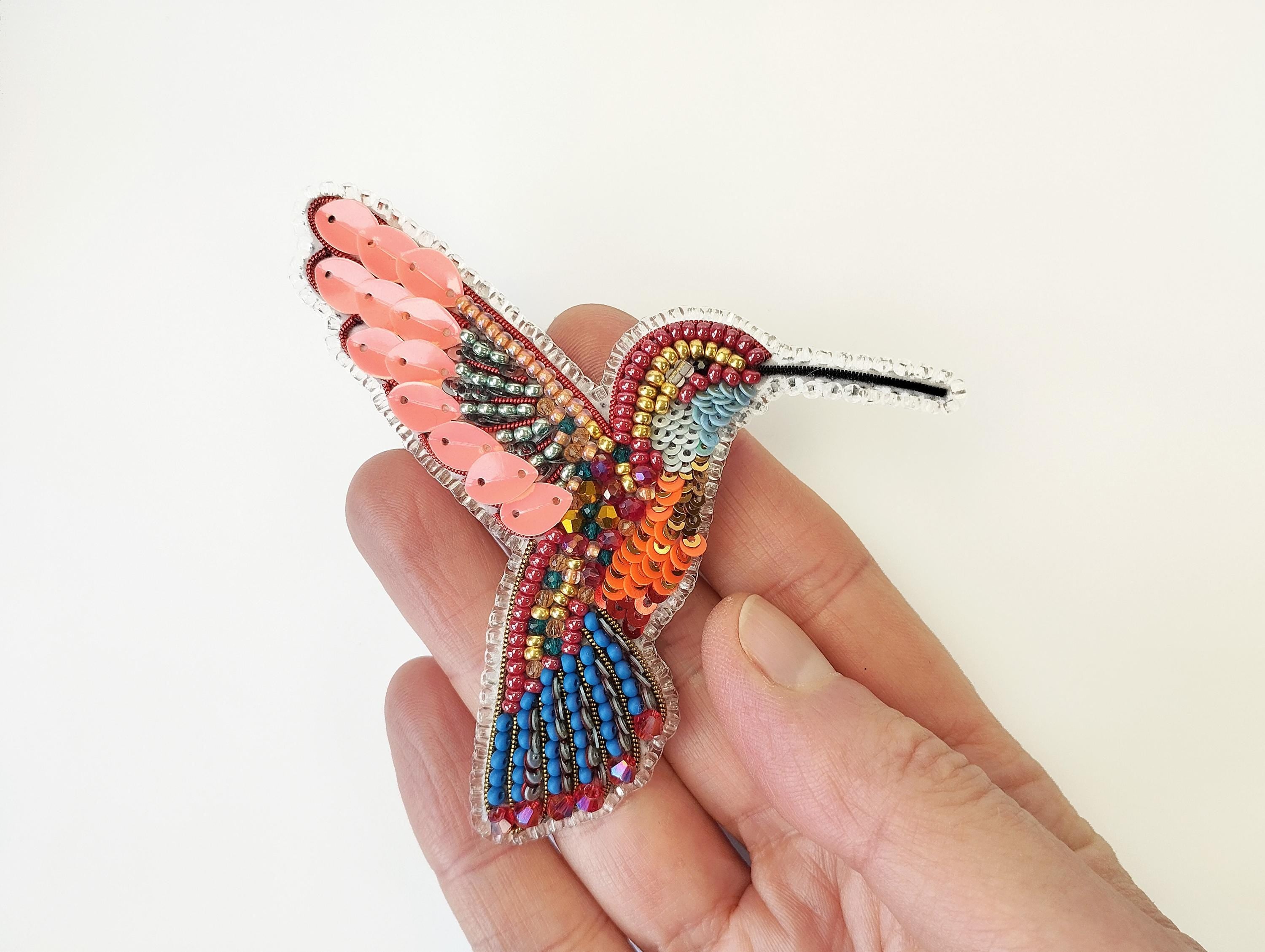a hand holding a colorful beaded bird brooch