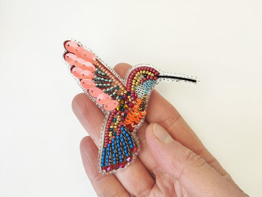 a hand holding a colorful beaded bird brooch