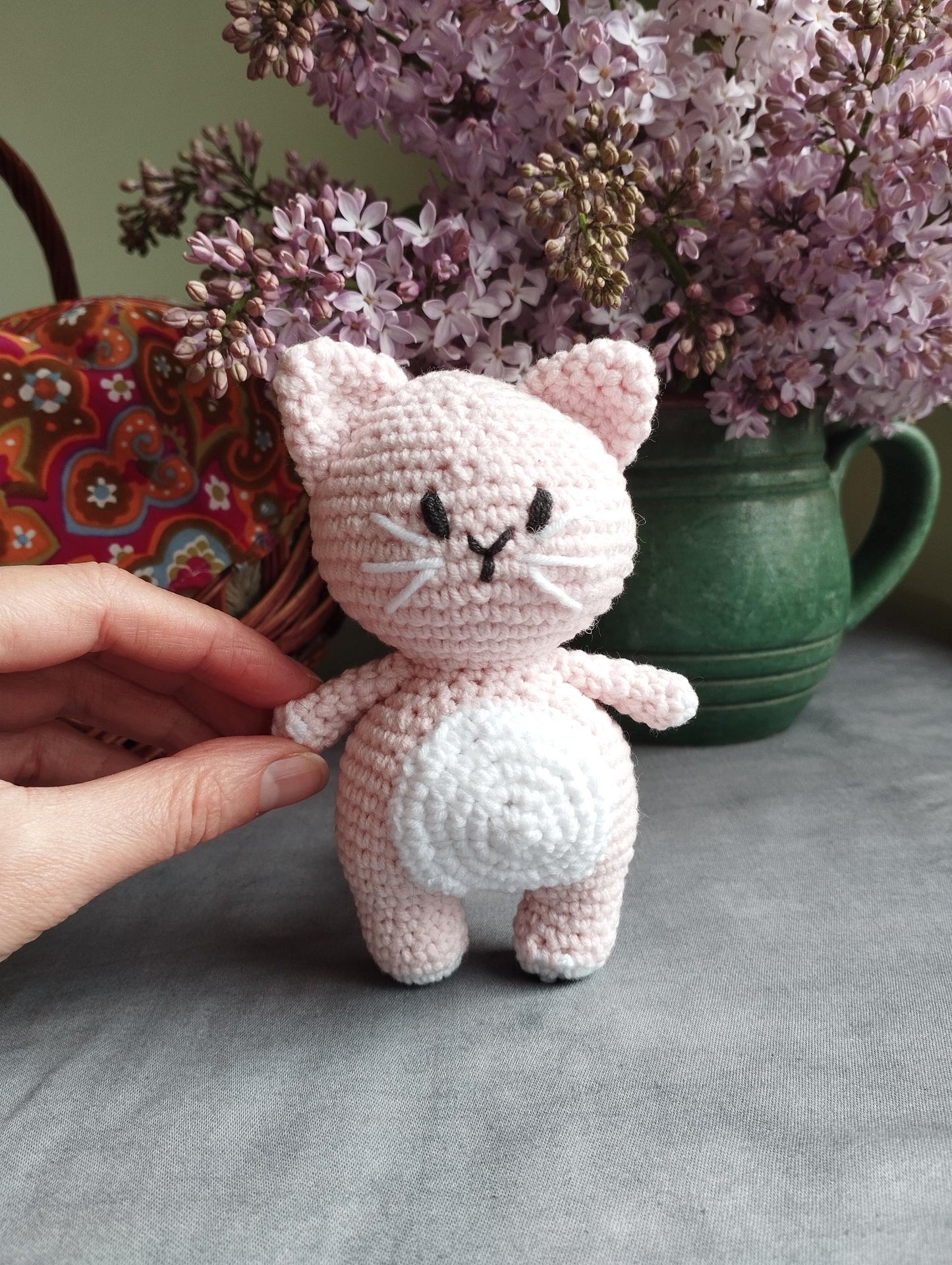a crocheted cat sitting on a table next to a vase of flowers