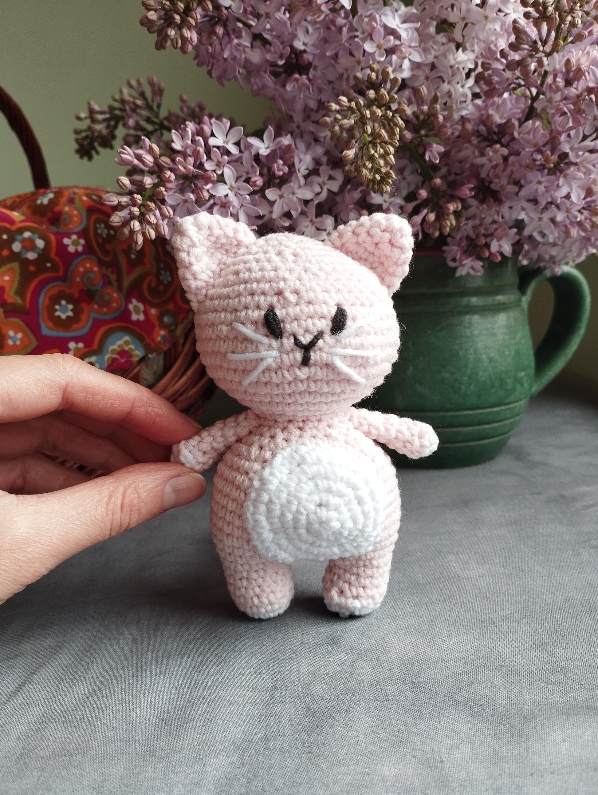 a crocheted cat sitting on a table next to a vase of flowers