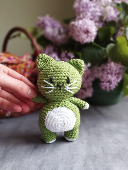 a crocheted green cat sitting next to a basket of flowers