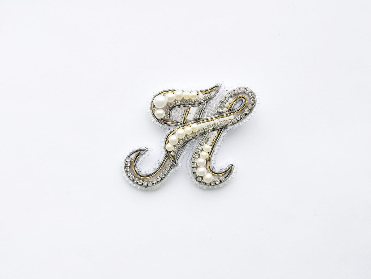 a decorative letter 'H' made of beads and pearls, set against a plain white background.
