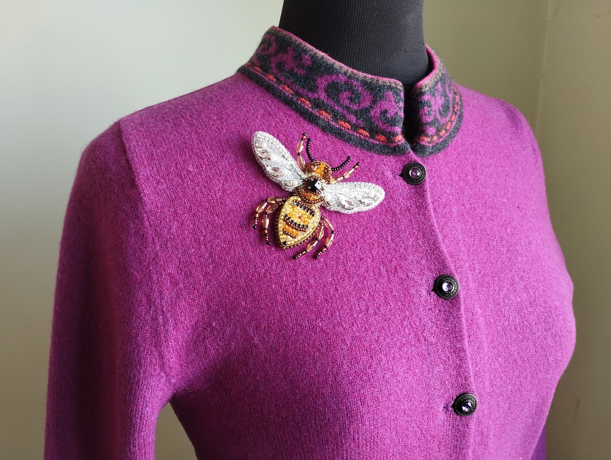 A mannequin wearing a purple cardigan with a decorative bee embroidered on the front.