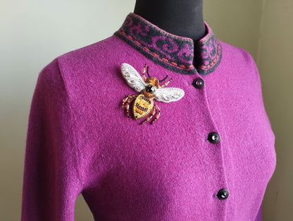 A mannequin wearing a purple cardigan with a decorative bee embroidered on the front.