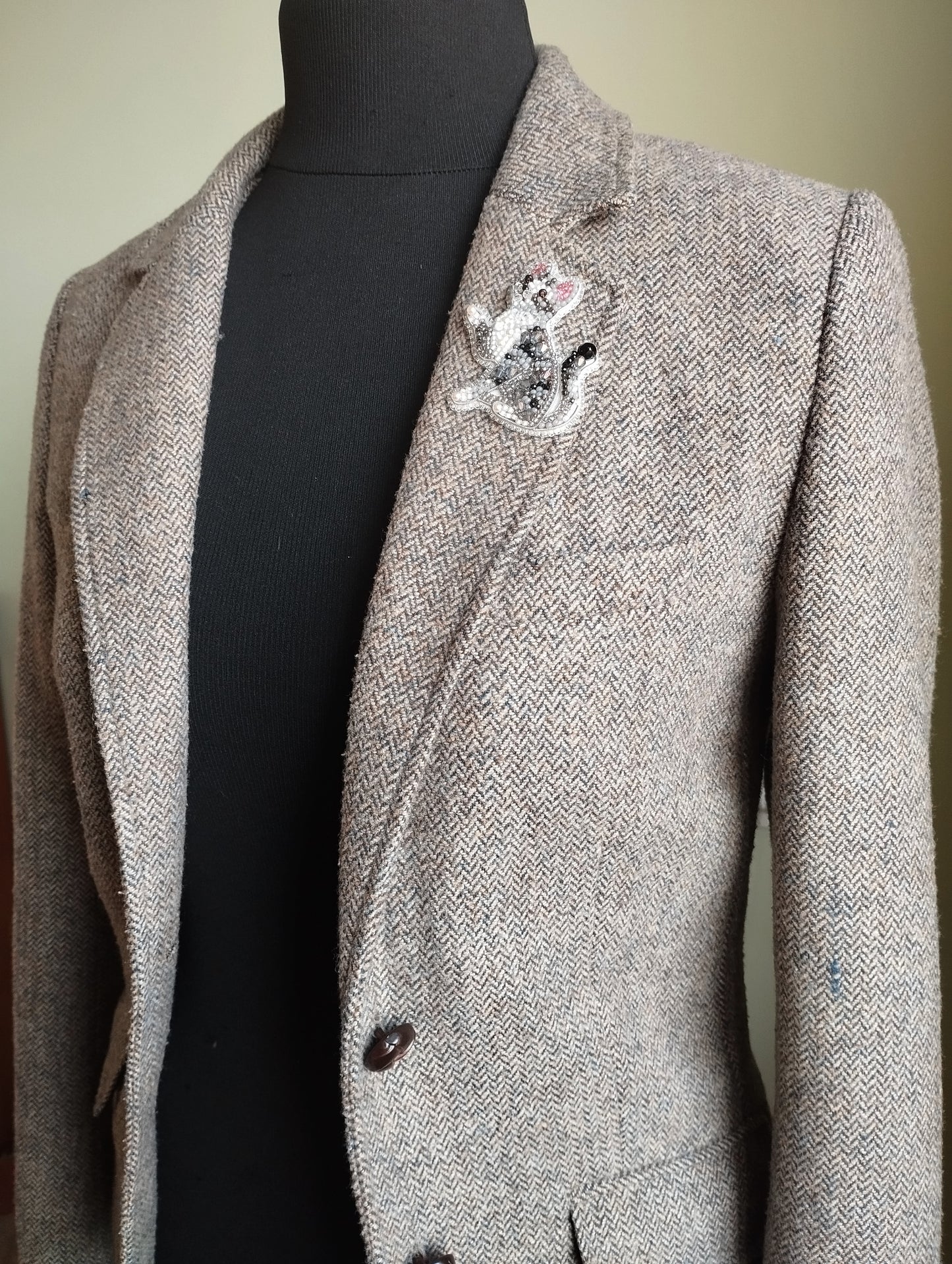 A mannequin wearing a gray tweed blazer with a black turtleneck sweater underneath.