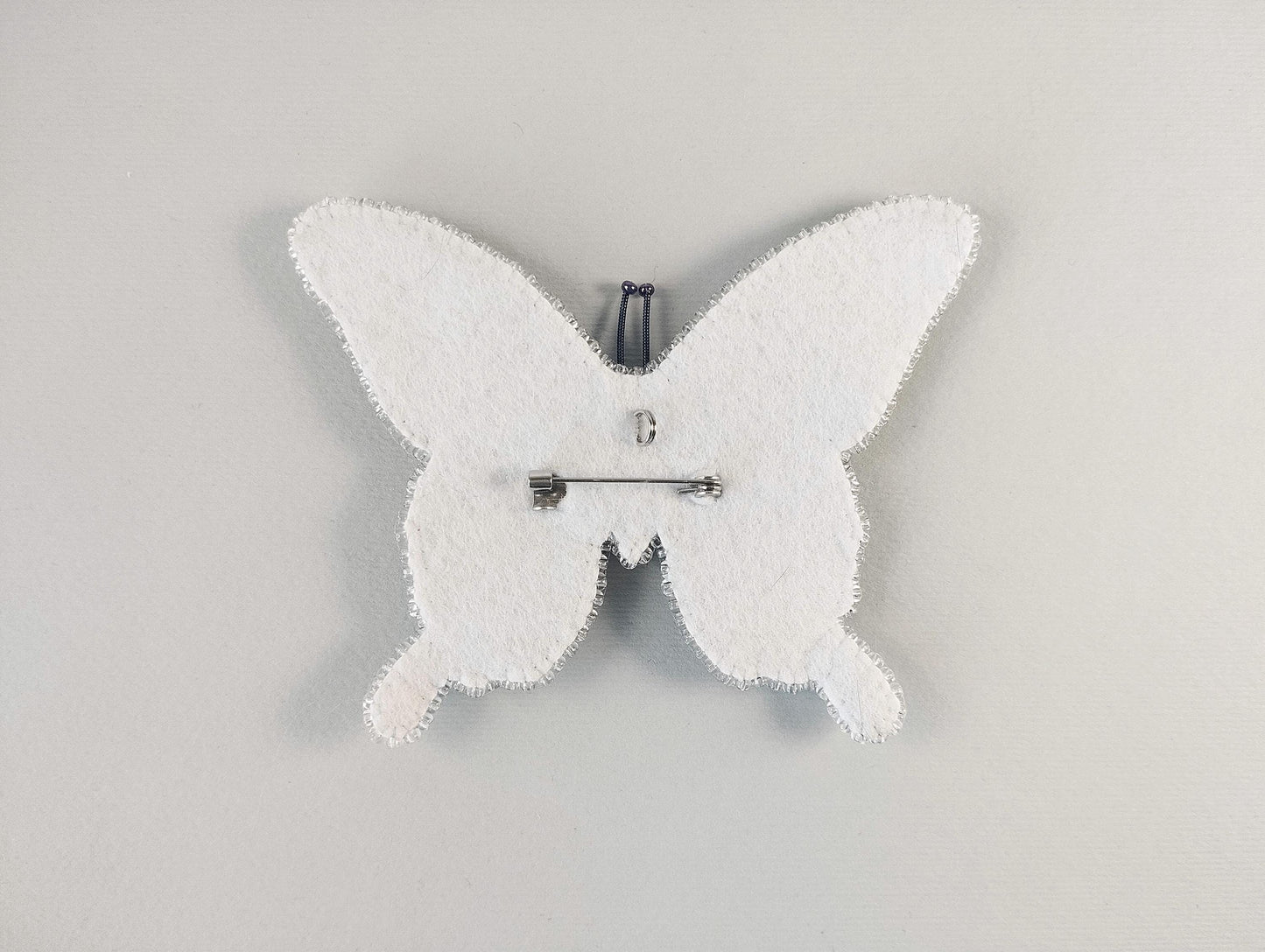 A white butterfly-shaped object with a pin attached to it, set against a plain white background.