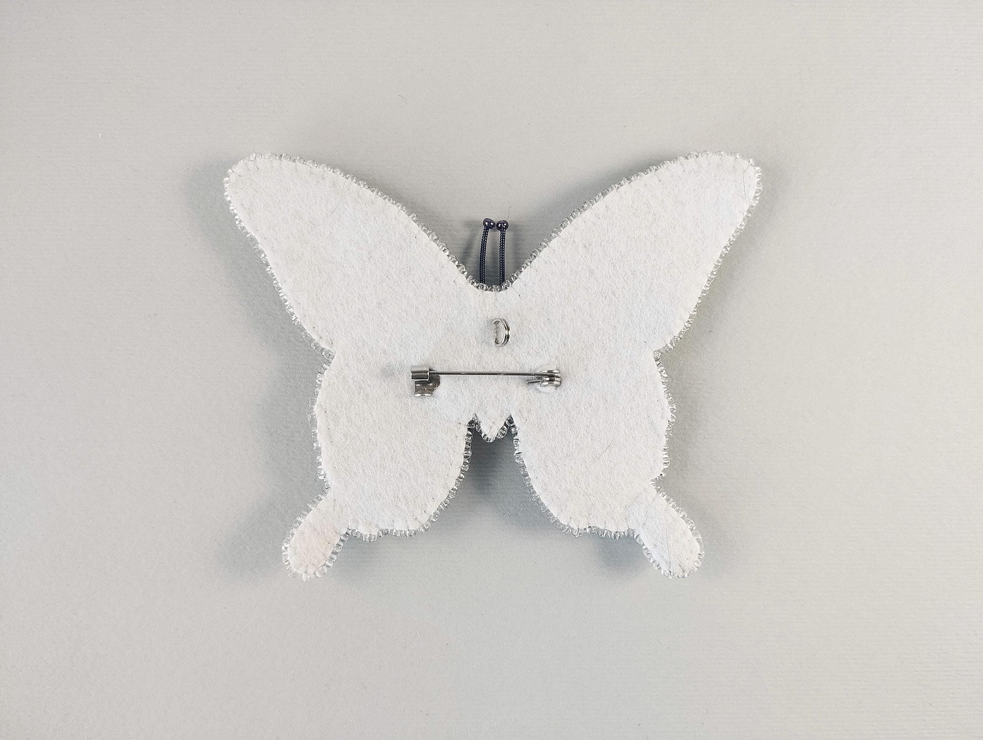 A white butterfly-shaped object with a pin attached to it, set against a plain white background.