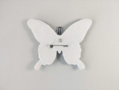 A white butterfly-shaped object with a pin attached to it, set against a plain white background.