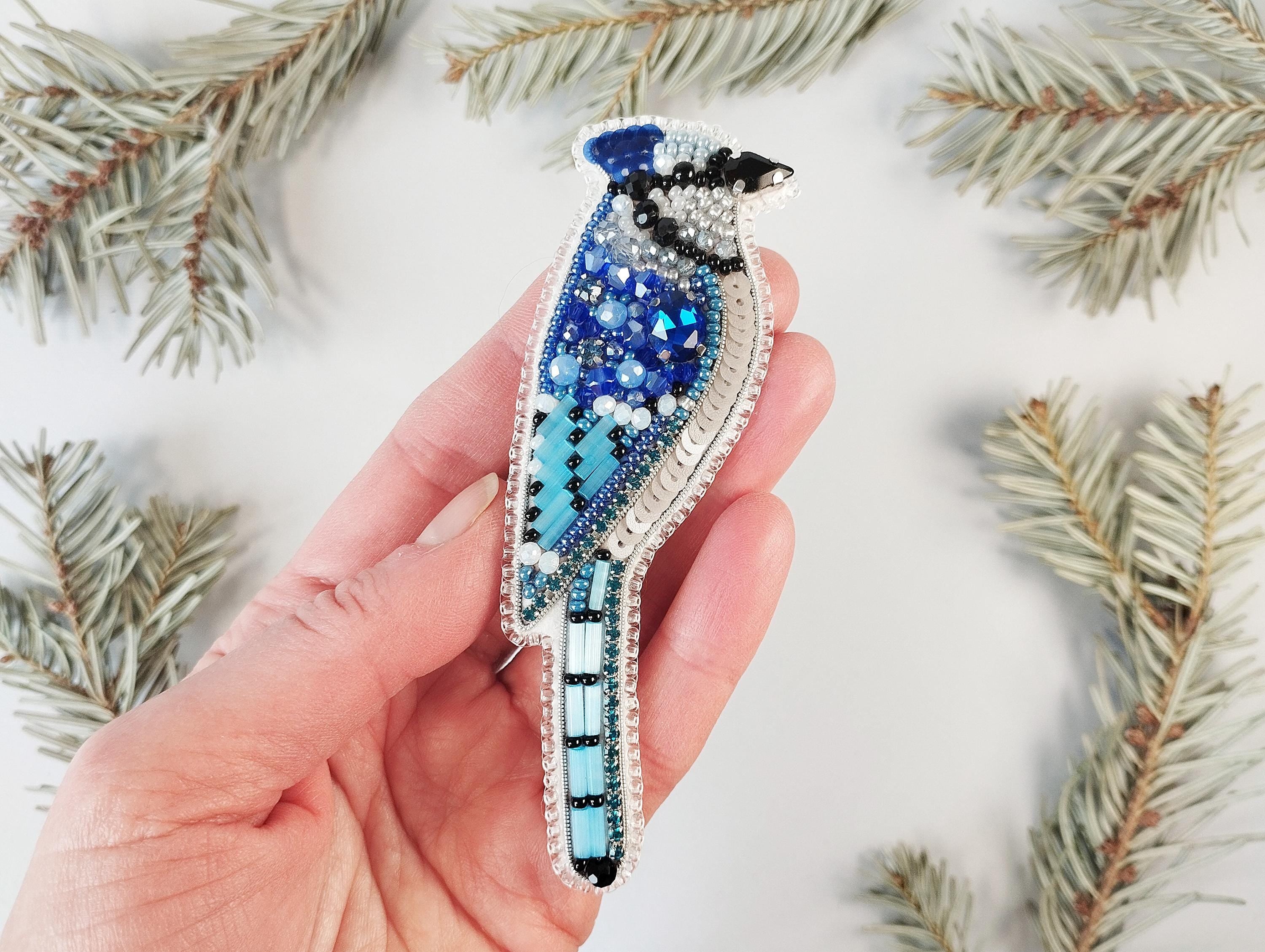 a hand holding a brooch with a blue bird on it