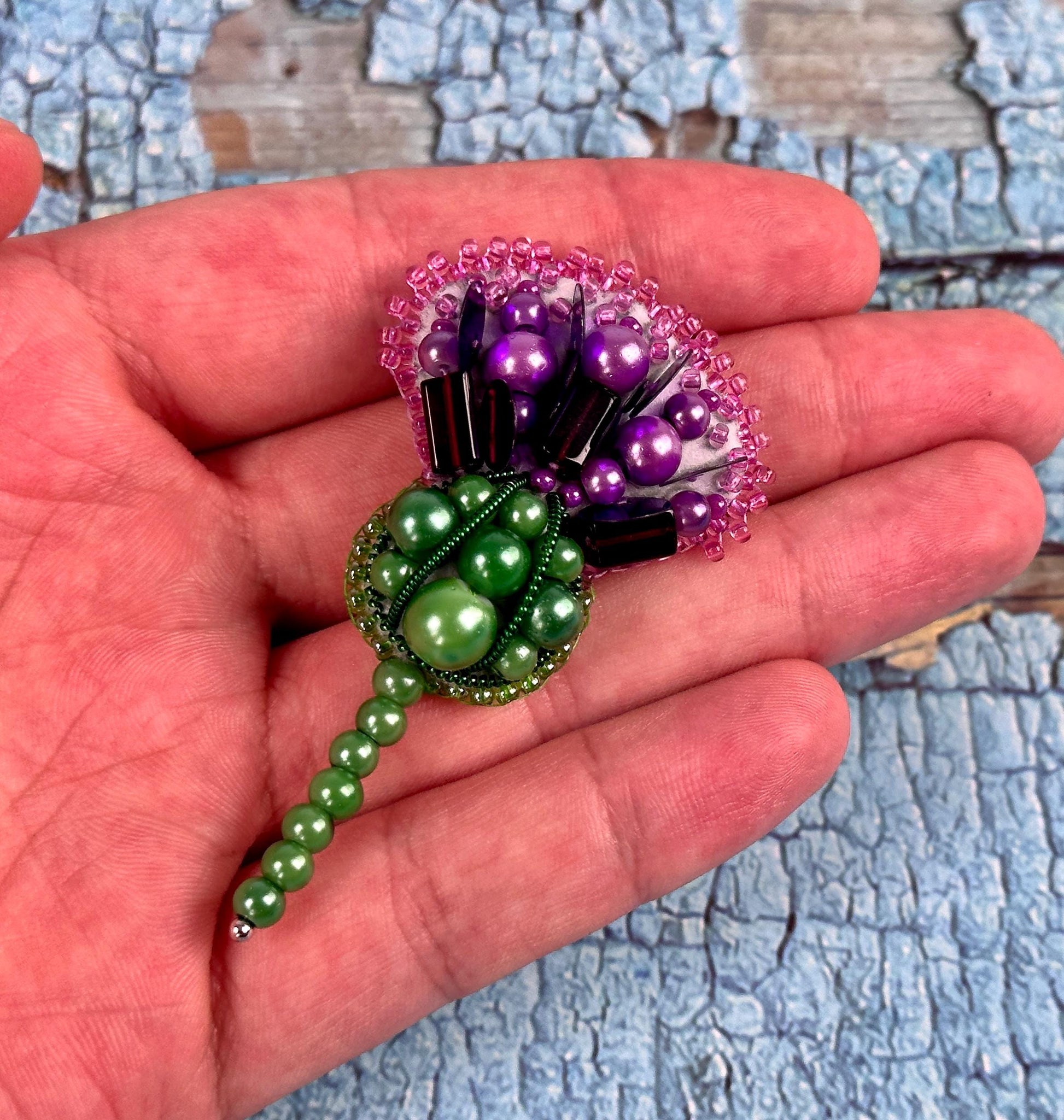 a hand holding a small green and purple flower brooch