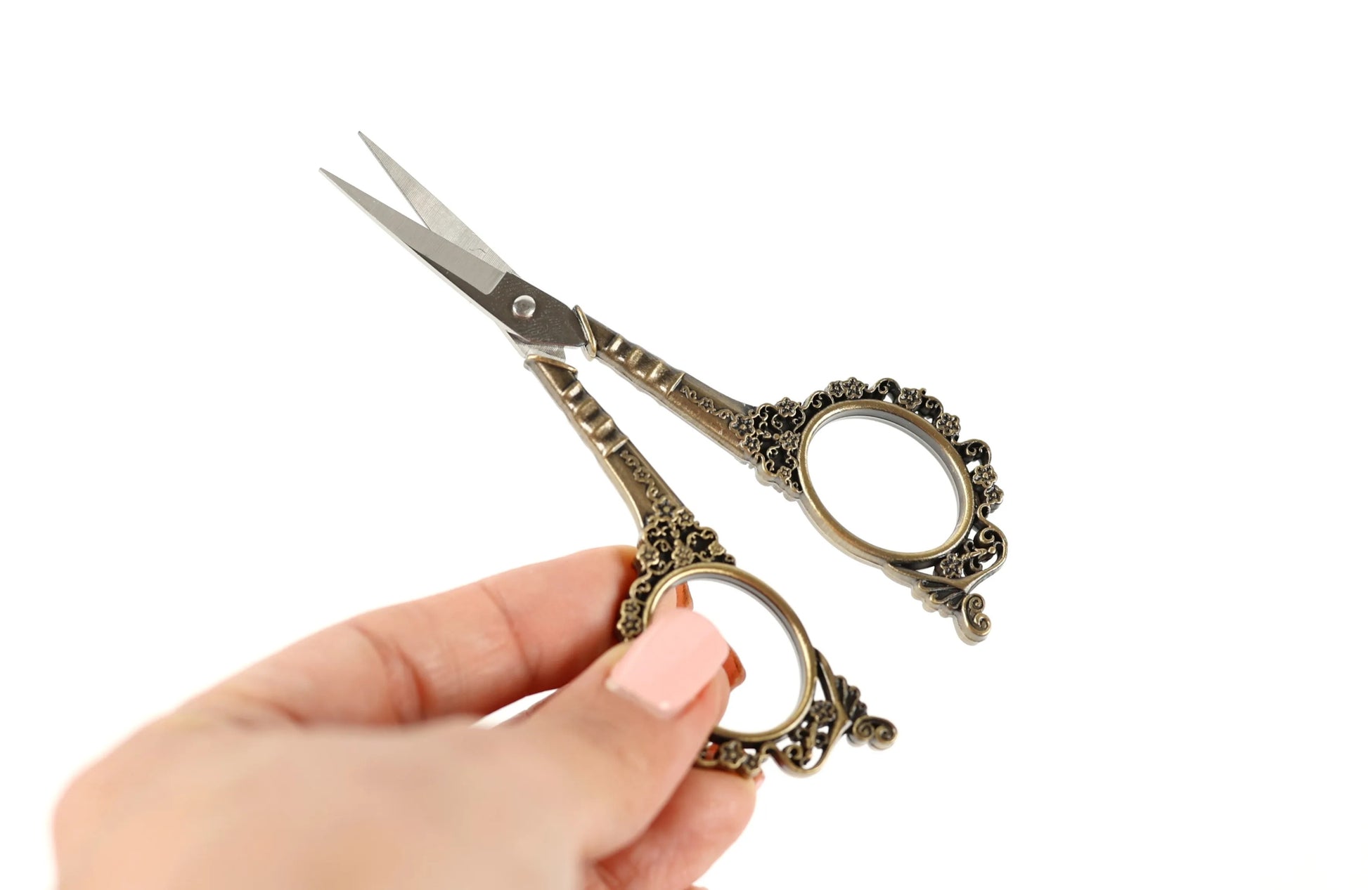 A hand holding a pair of ornate scissors against a white background.