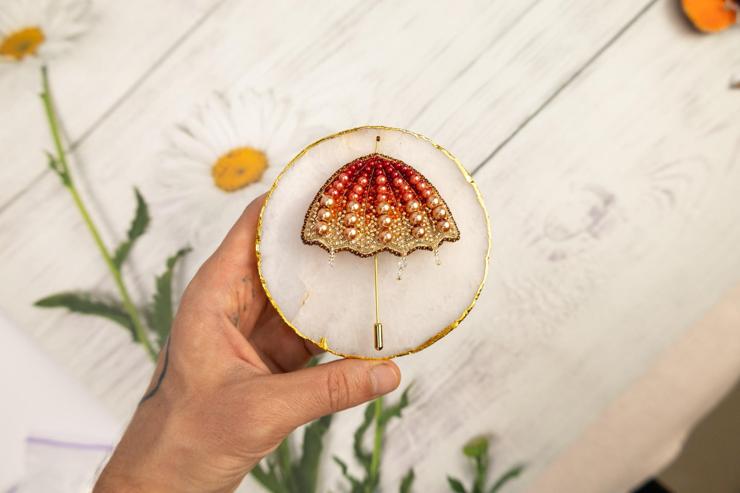 a hand holding a small white and gold brooch