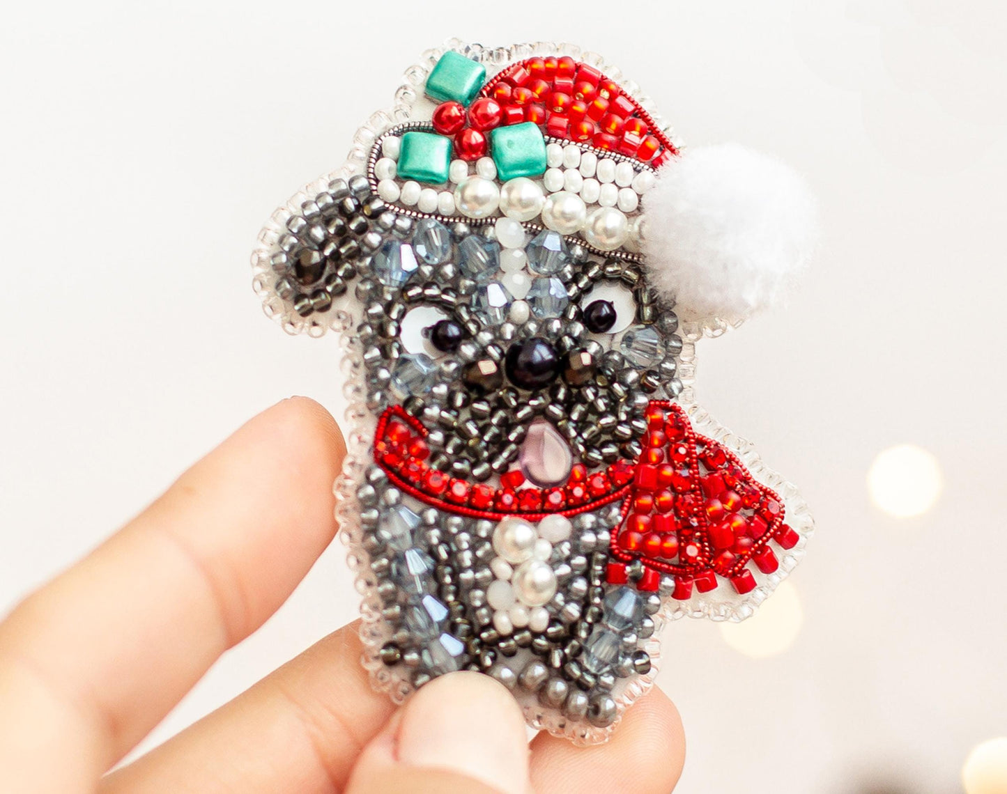A hand holding a small, intricately beaded ornament in the shape of a dog wearing a Santa hat and scarf.