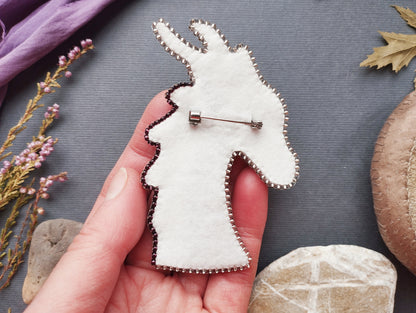 A hand holding a white pin-like object with a decorative design, surrounded by various natural elements such as flowers, leaves, and rocks.