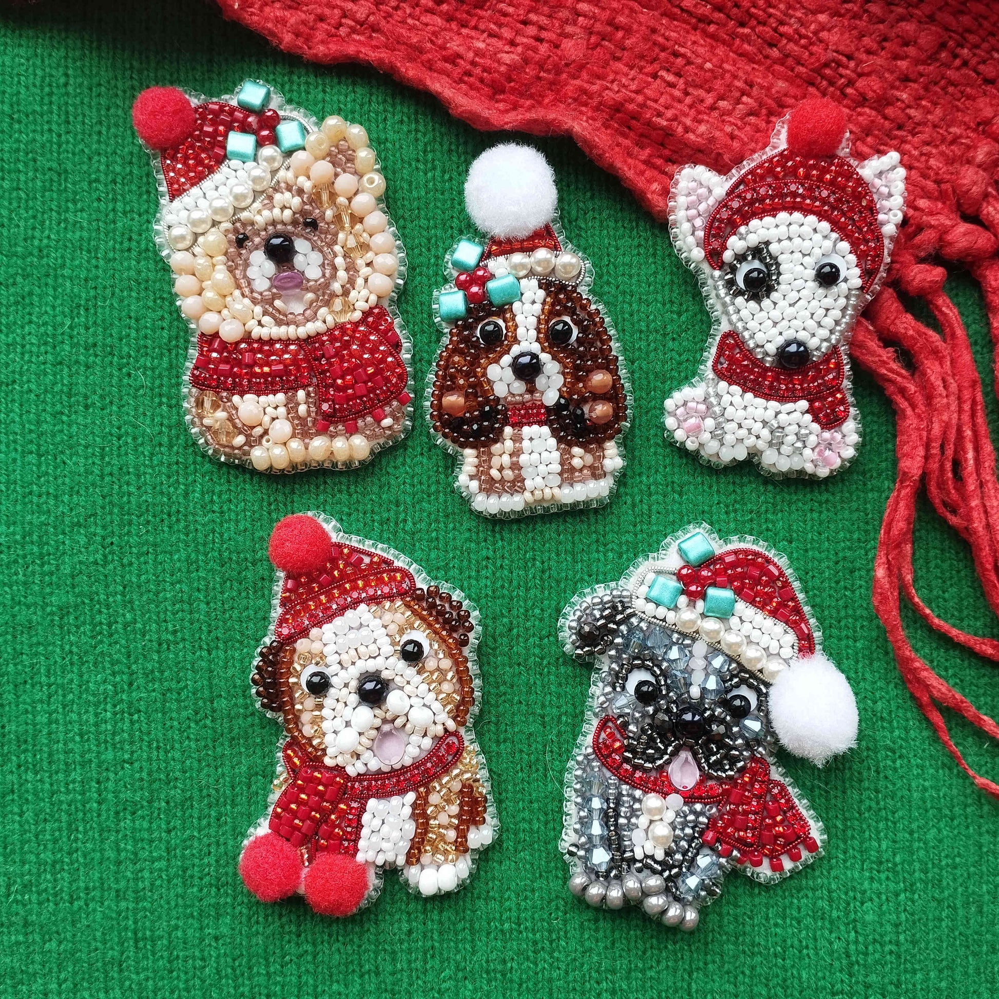 five beaded or embroidered dog or puppy brooches in various colors and styles, placed on a green background.