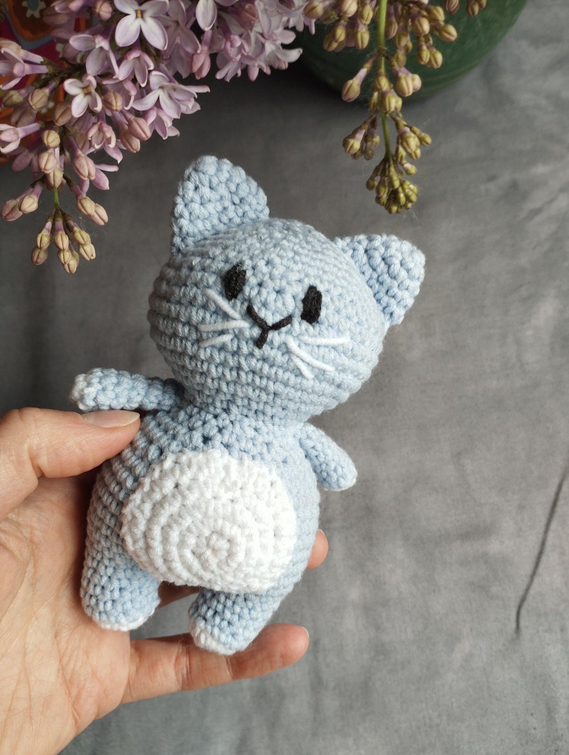 a hand holding a small blue crocheted cat