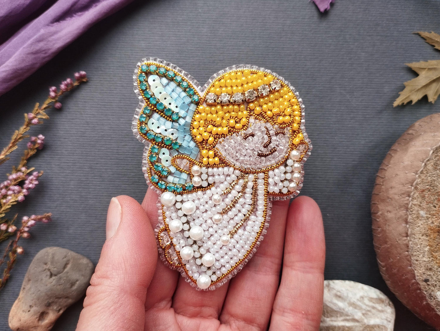 A hand holding a decorative beaded piece featuring a butterfly-like design with a smiling face.
