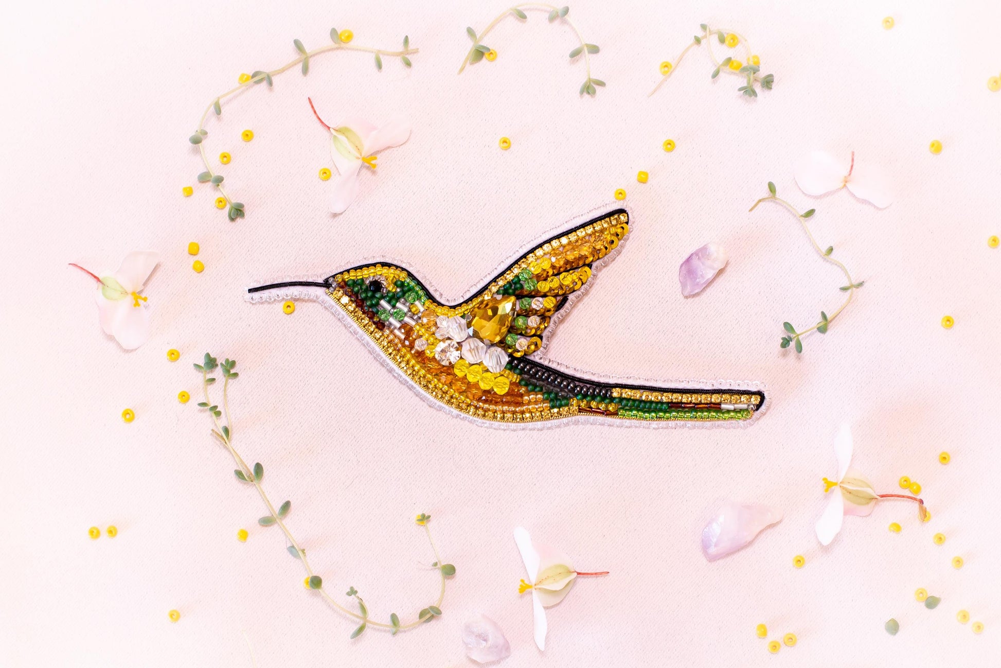 a vibrant, hand-embroidered hummingbird with a yellow body, green wings, and a black beak, surrounded by delicate white flowers and green leaves.