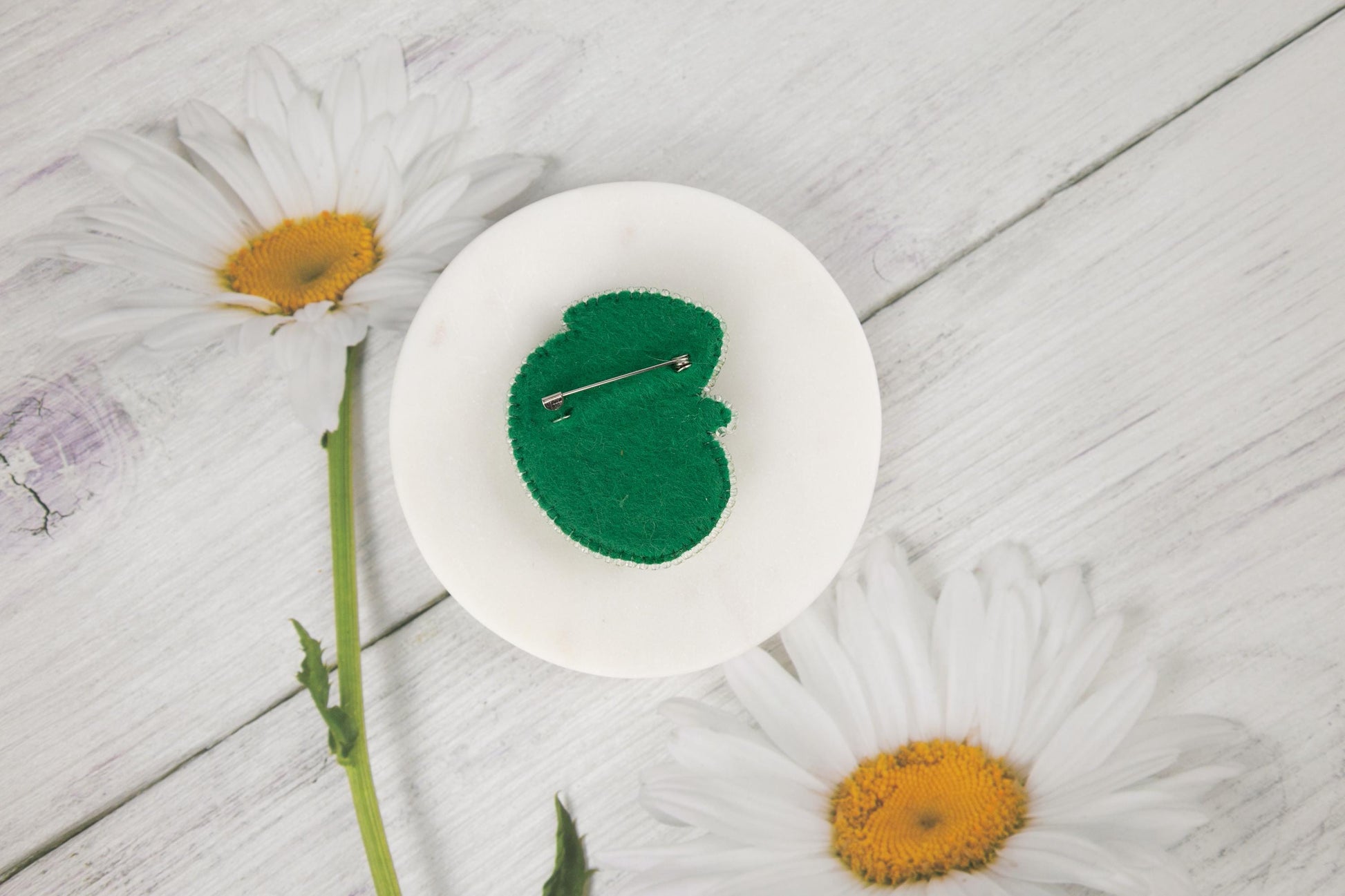 a white plate with a green leaf on it next to daisies