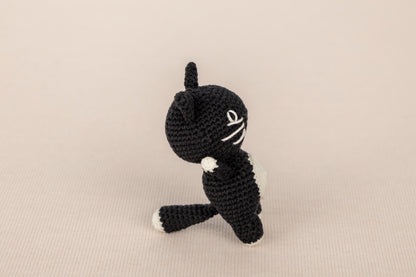 a crocheted black and white cat sitting on its hind legs