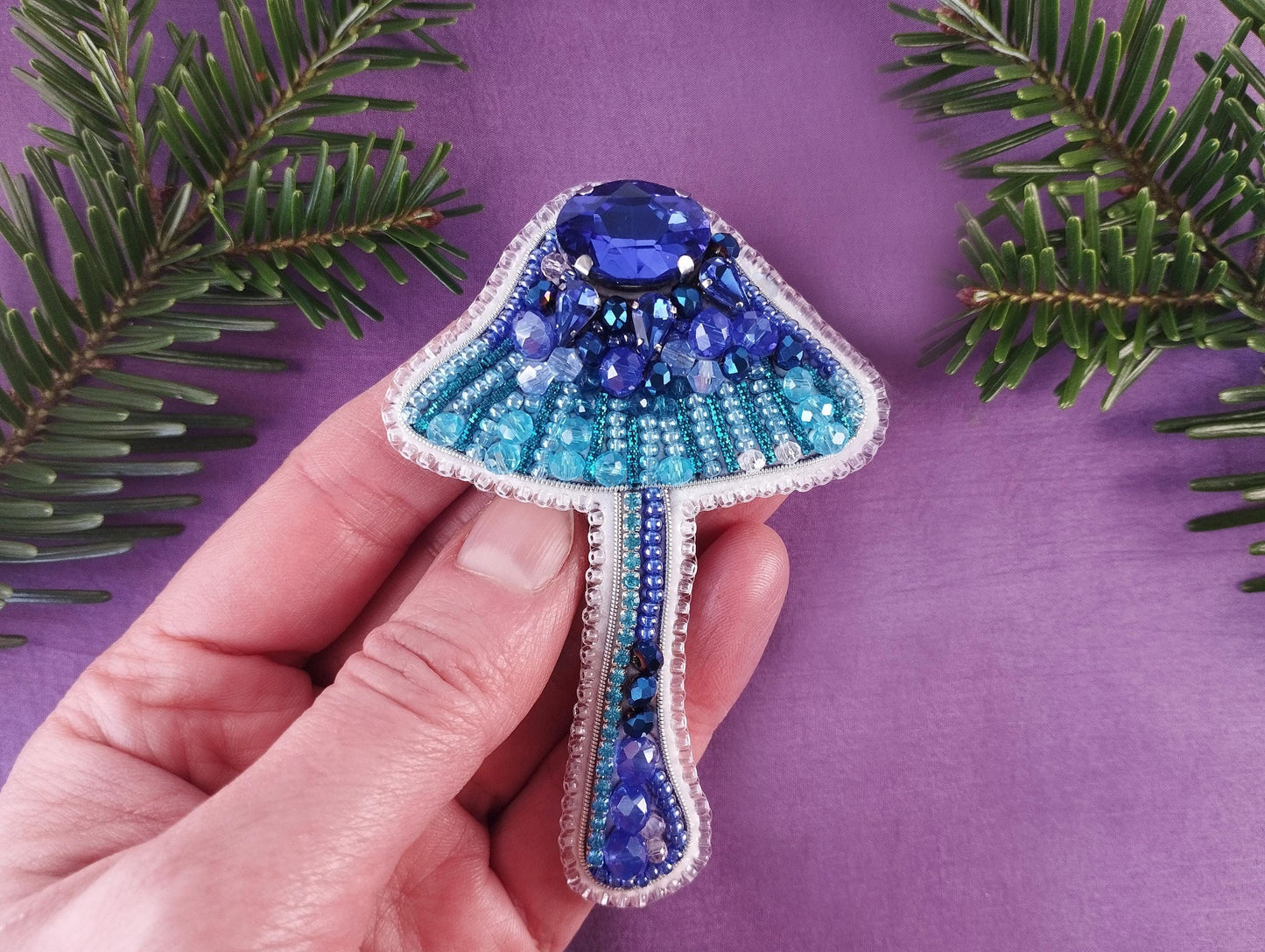 a hand holding a blue and white beaded brooch