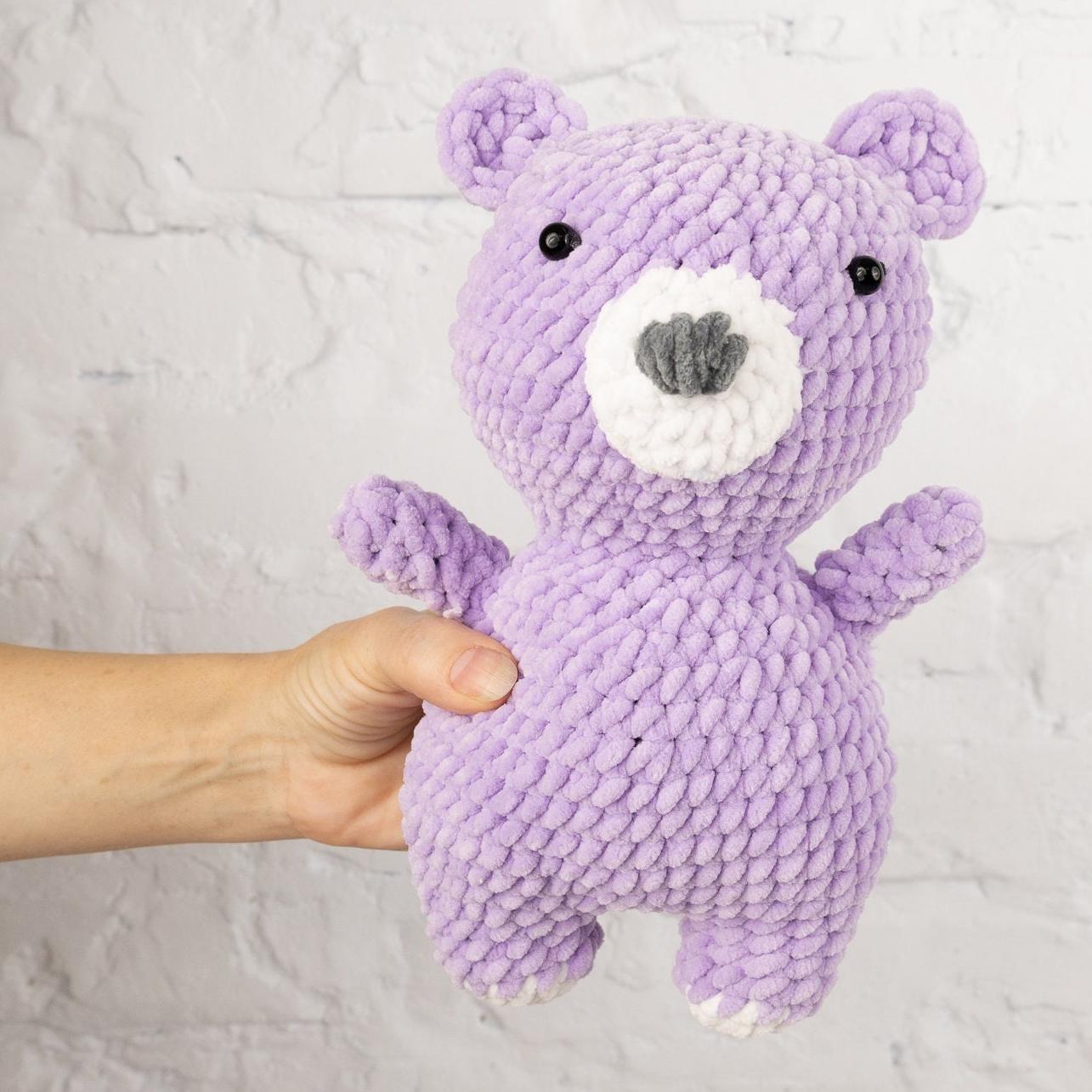 a purple knitted teddy bear standing on its hind legs