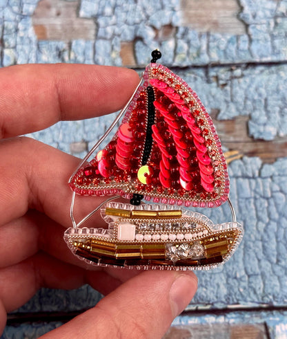 a hand holding a small sail boat ornament