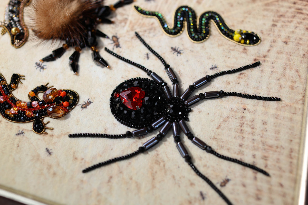 a close-up of a detailed embroidered spider with a red heart at its center, surrounded by various other embroidered insects and animals.