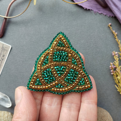 A hand holding a triangular beaded object with a green and gold color scheme.