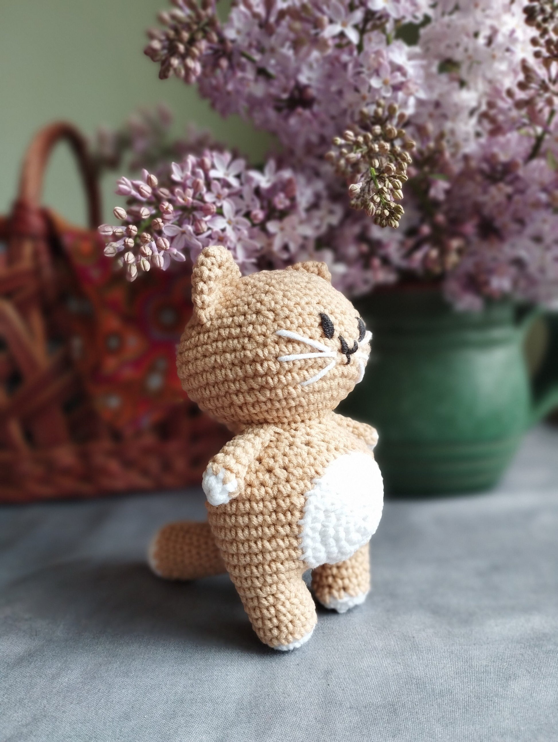 a crocheted cat sitting next to a basket of flowers