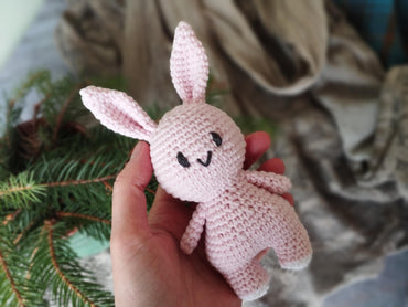 a hand holding a small pink crocheted bunny