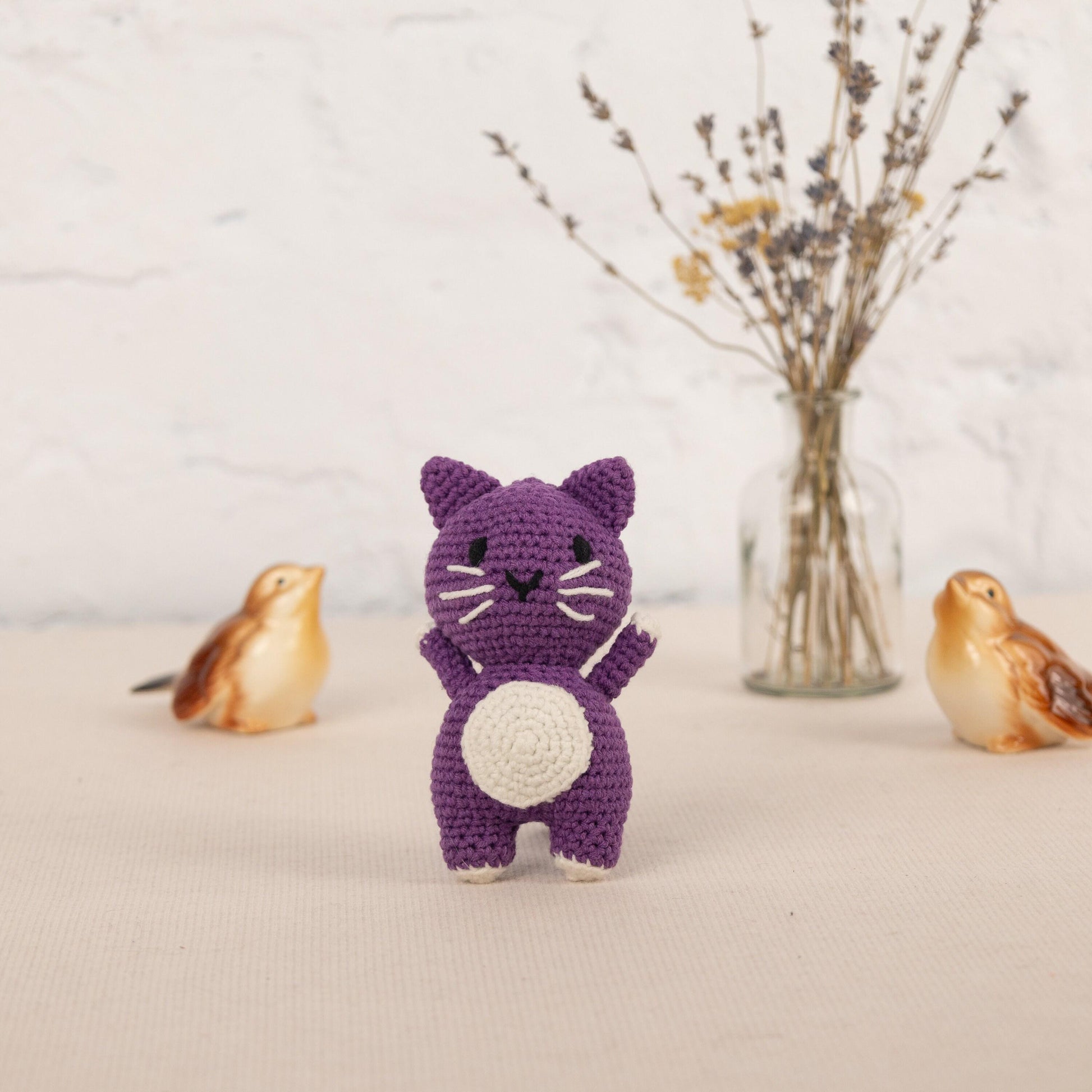 a crocheted cat standing next to a vase of flowers