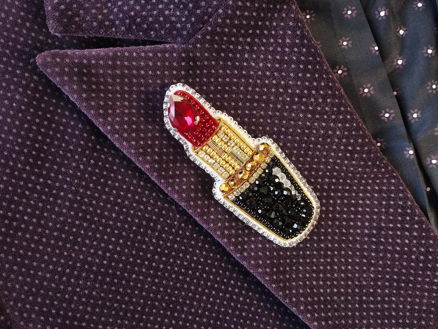 A close-up image of a purple jacket with a red and gold brooch featuring a red lipstick design.