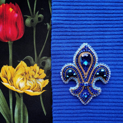 a close-up of a blue fabric with a decorative blue and gold brooch in the center, and a red tulip flower on the left side.