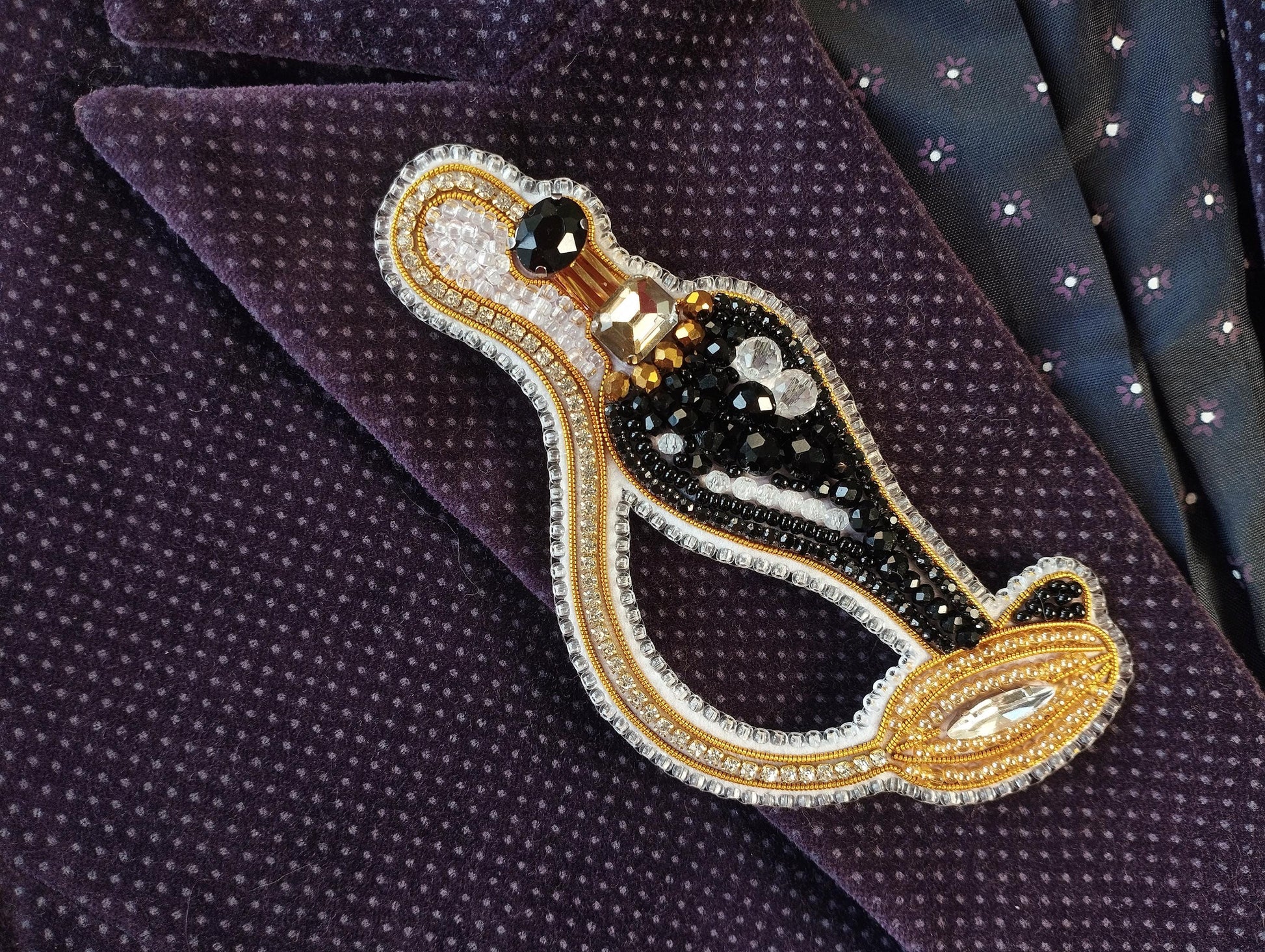 A close-up image of a decorative brooch or pin with a black and gold design, placed on a purple fabric with a polka dot pattern.