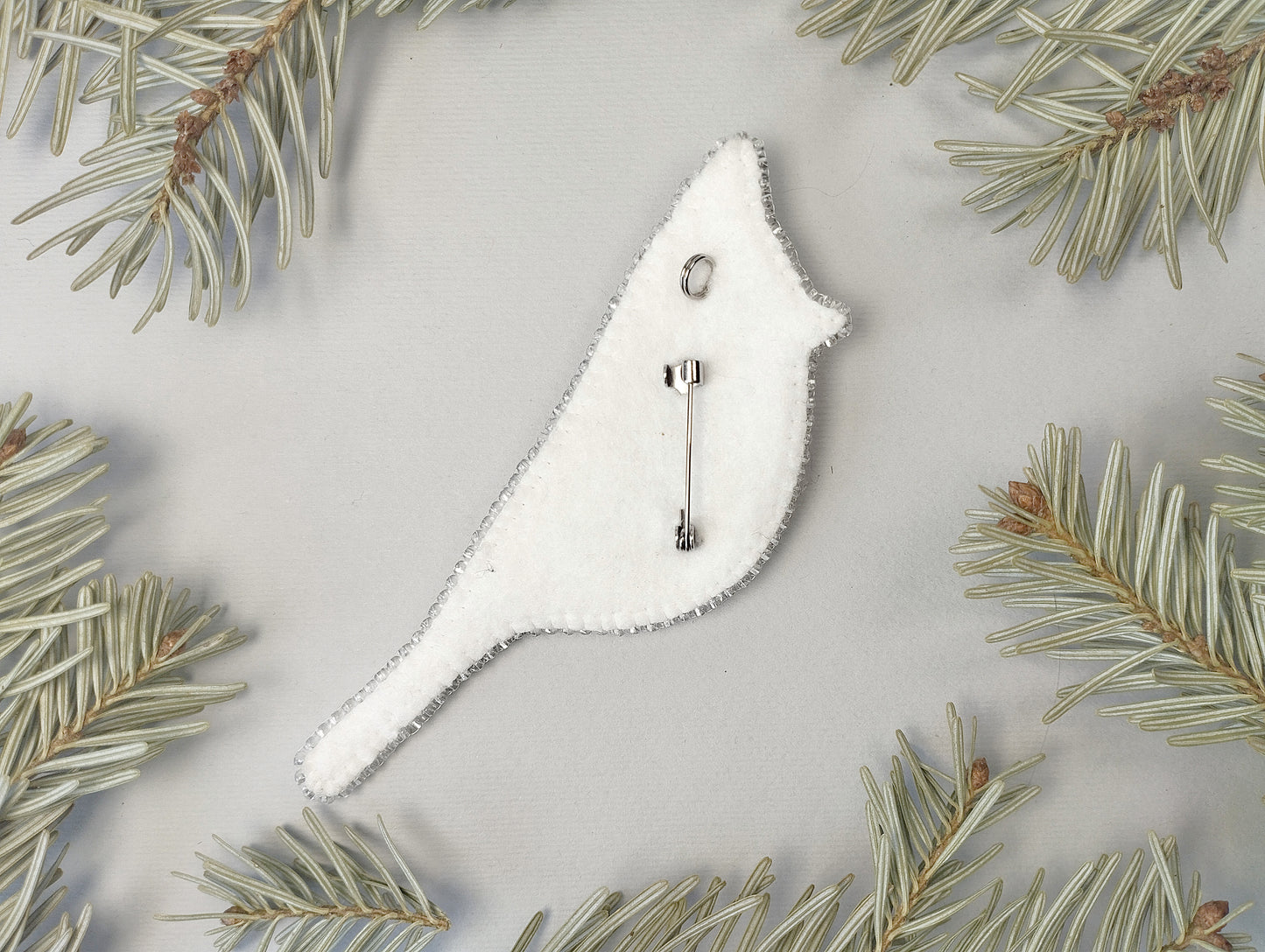 A white bird-shaped ornament is placed on a light grey background, surrounded by pine needles.