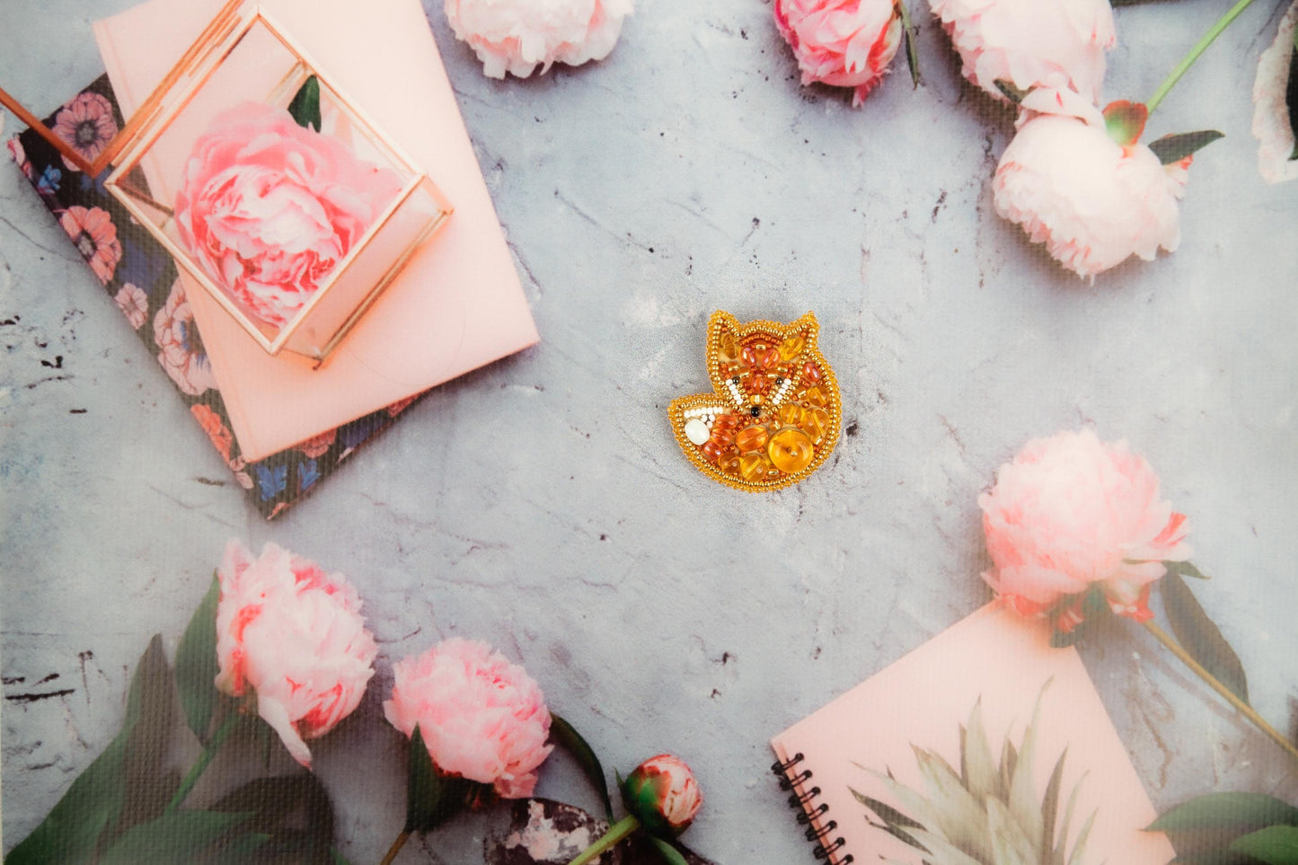 a gold brooch sitting on top of a table next to pink flowers