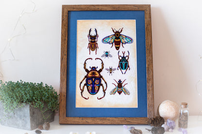a framed artwork of colorful insects, including a large dragonfly, a bee, and several other insects, displayed on a white surface.