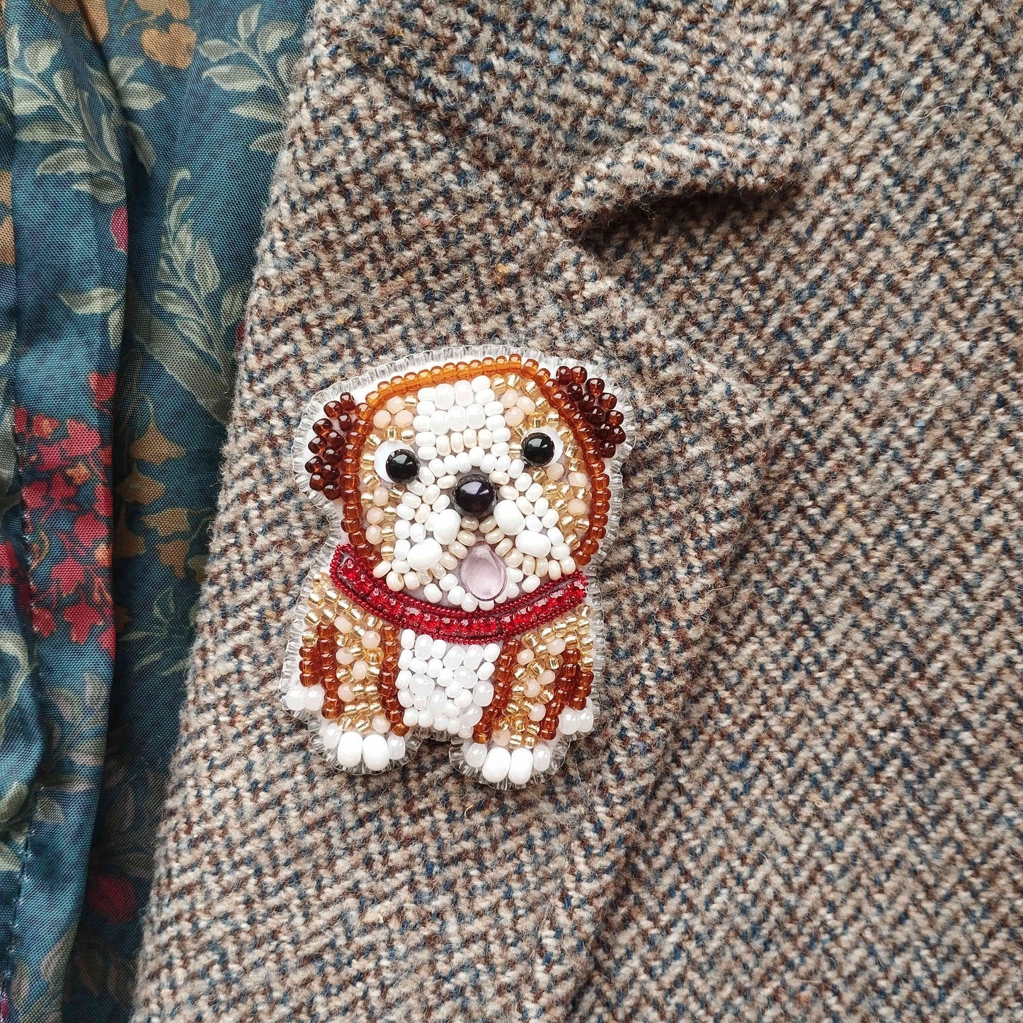 A close-up of a beaded embroidered dog pin on a tweed fabric.