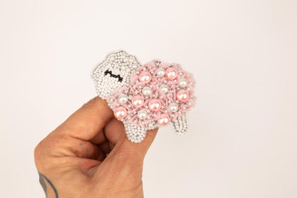 a hand is holding a beaded sheep brooch