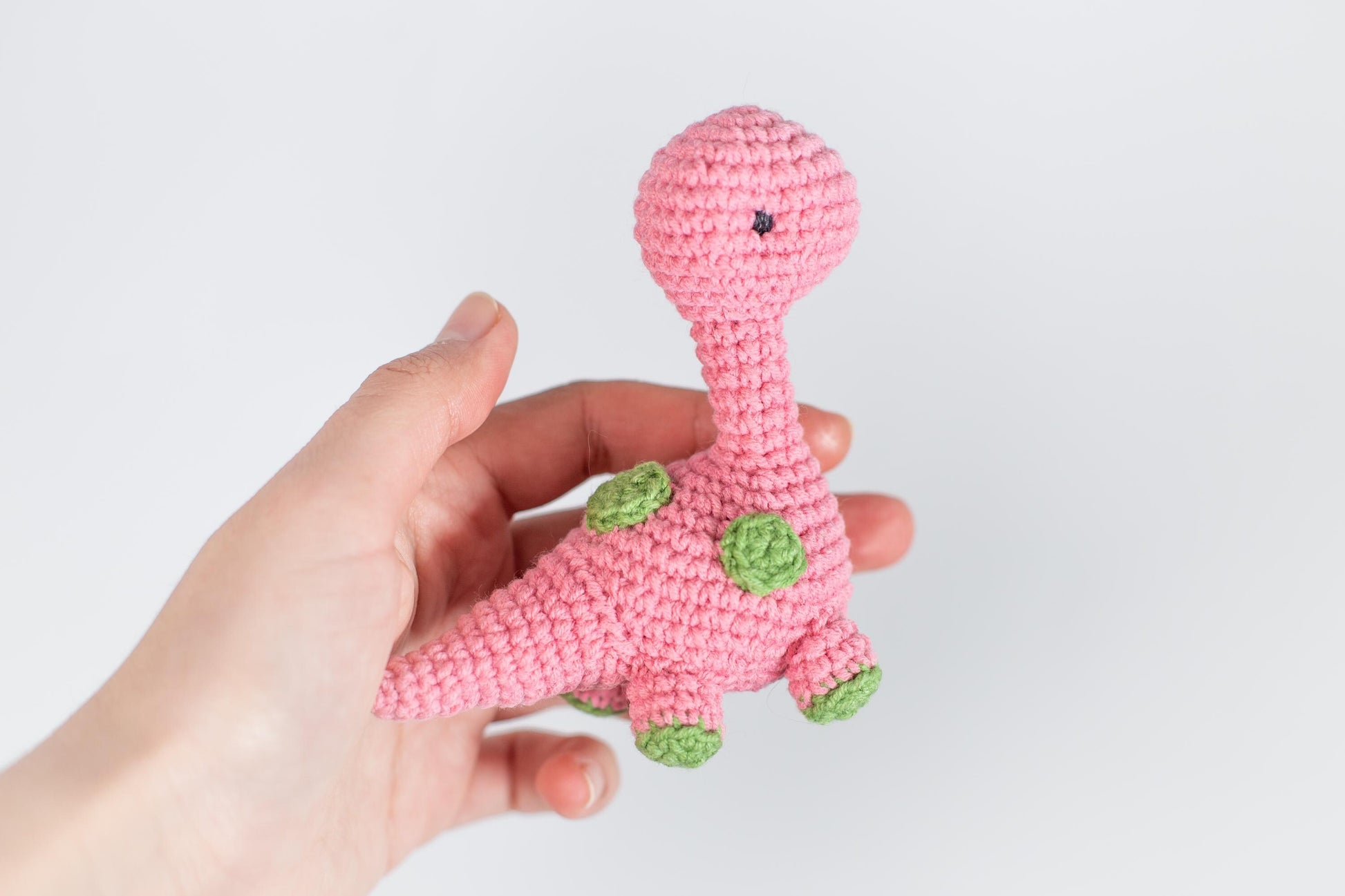 a hand holding a pink crocheted toy that looks like a giraffe