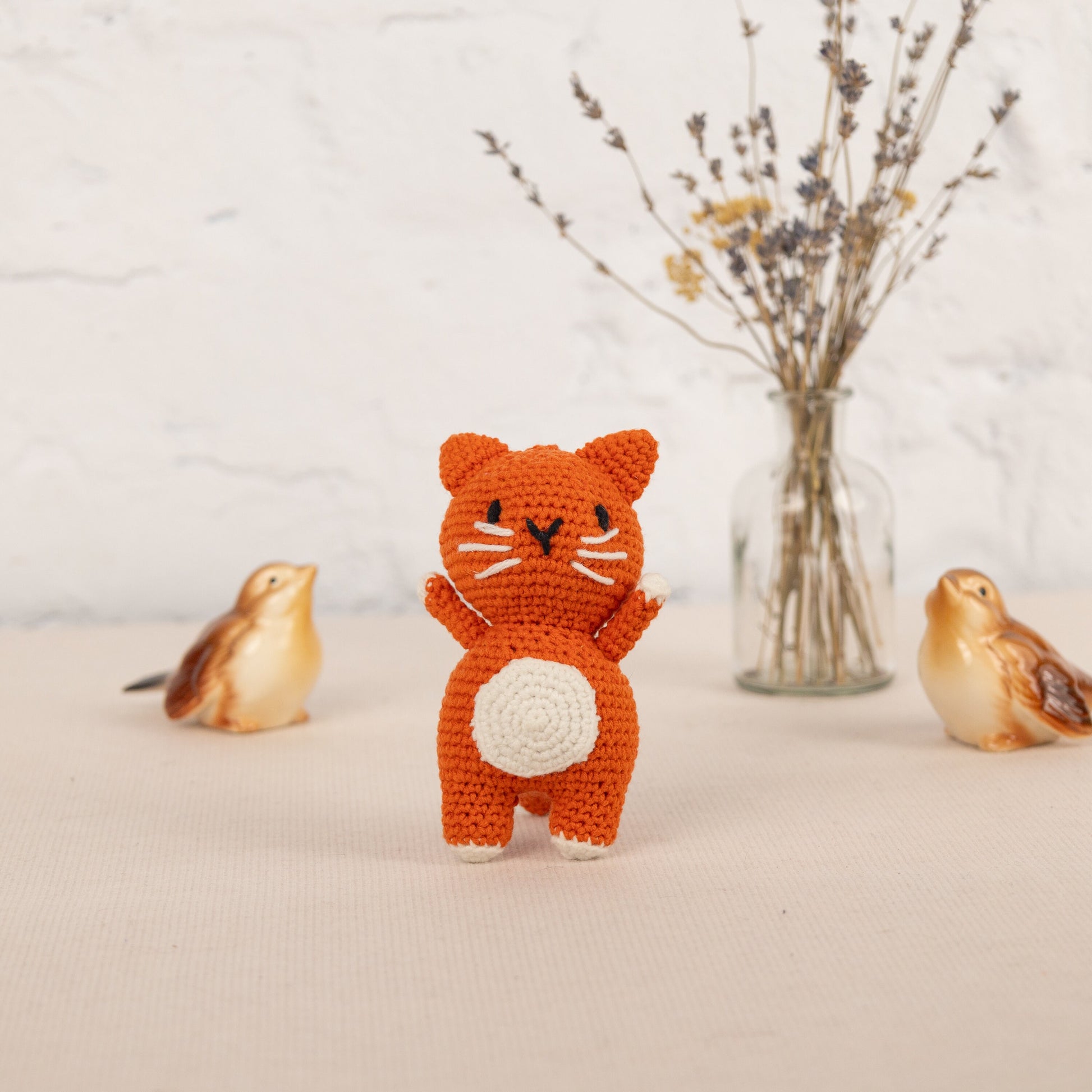 a small crocheted cat standing next to two small birds
