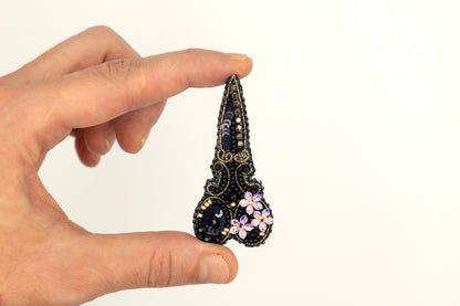 a hand holding a small black and pink brooch