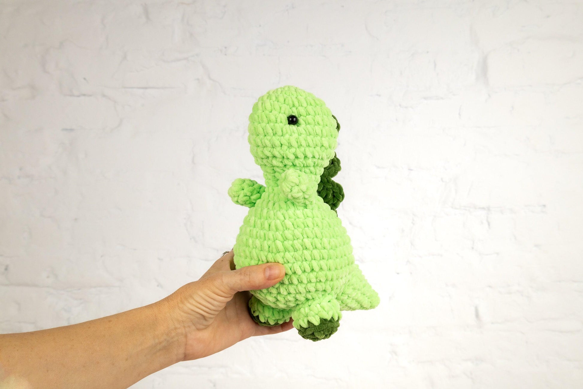 a hand holding a green crocheted stuffed animal