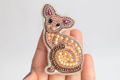 A hand holding a decorative beaded cat pin.