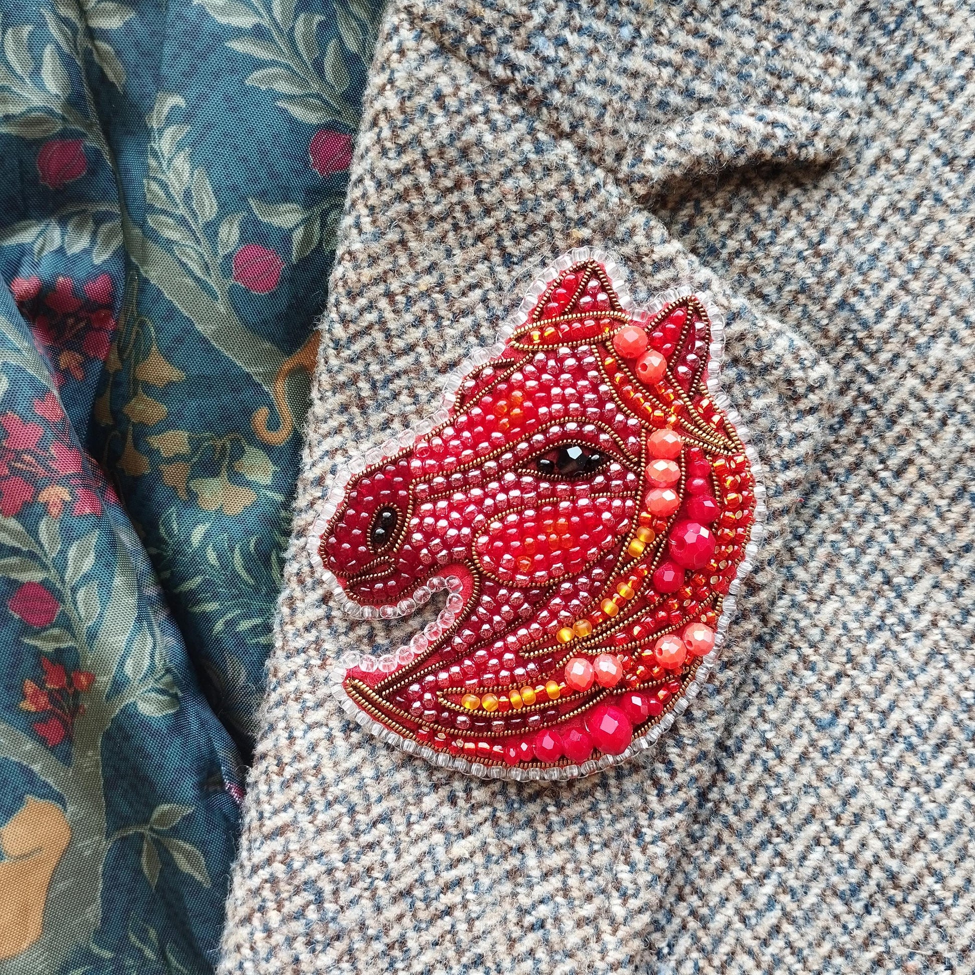a close-up of a red and gold beaded embroidered piece of clothing, which appears to be a brooch or pin.