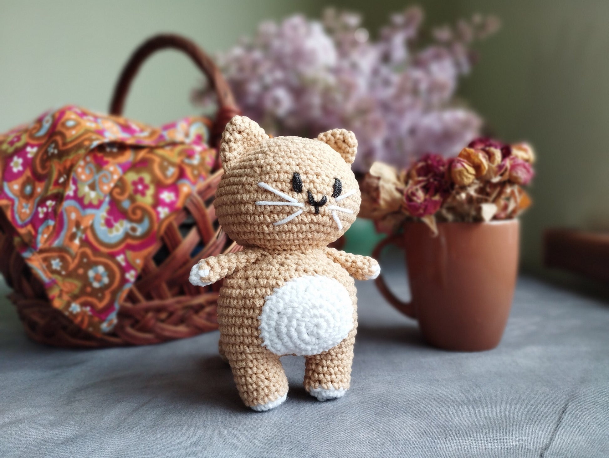 a crocheted cat sitting next to a basket of flowers
